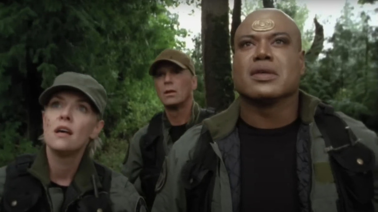 Samantha Carter from Amanda Taber stands alongside Jacques O'Neill from Richard Dean Anderson and Christopher Godz in a forest in Stargit SG-1