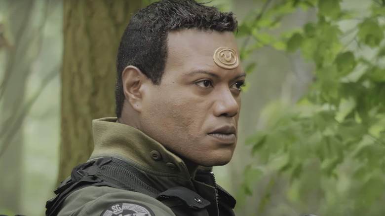 Christopher Judge's Teal'c stands against a green background of trees in Stargate SG-1