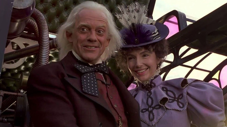 Doc Brown (Christopher Lloyd) stands next to Clara (Mary Steenburgen) in an elegant Western formal suit and lavender dress, inside the futuristic, steamer-style time-traveling train