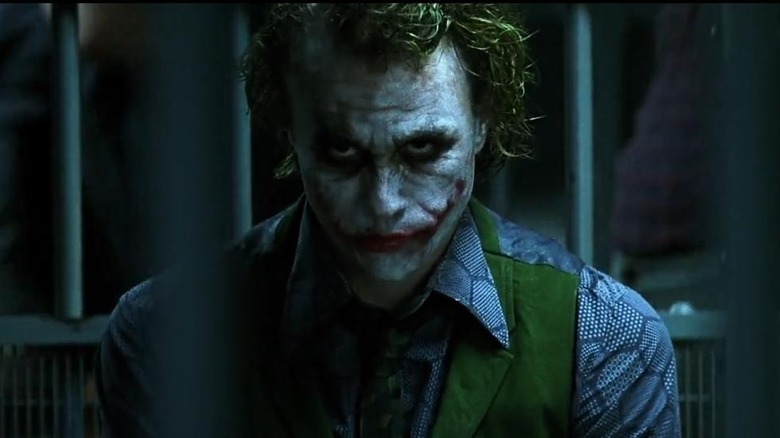 Heath Ledger as The Joker, looking menacingly off behind the camera while in a jail cell.