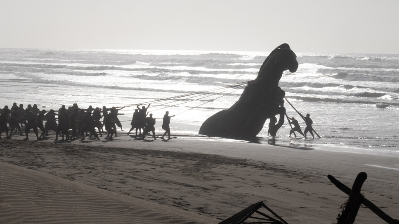 Trojan soldiers pulling a massive wooden horse from a beach in The Odyssey