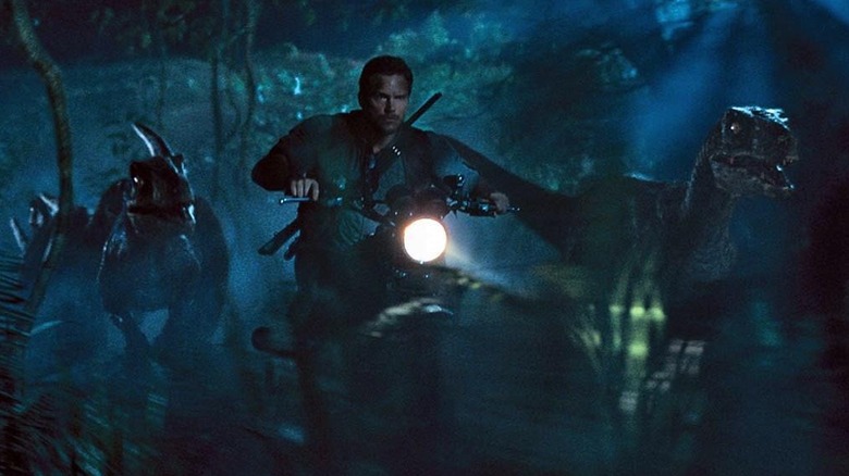 Chris Pratt as Owen Grady riding his motorcycle alongside some raptors in Jurassic World