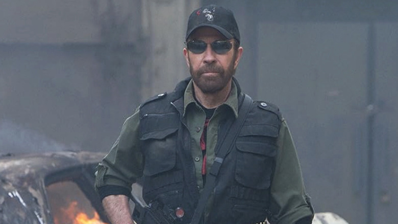 Chuck Norris as Booker walking in front of a burning car in The Expendables 2