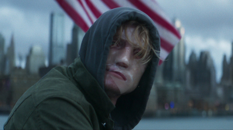 Tom Rhys Harries as Matt Hagen sittiing by an American flag with bandages on his face in Clayface