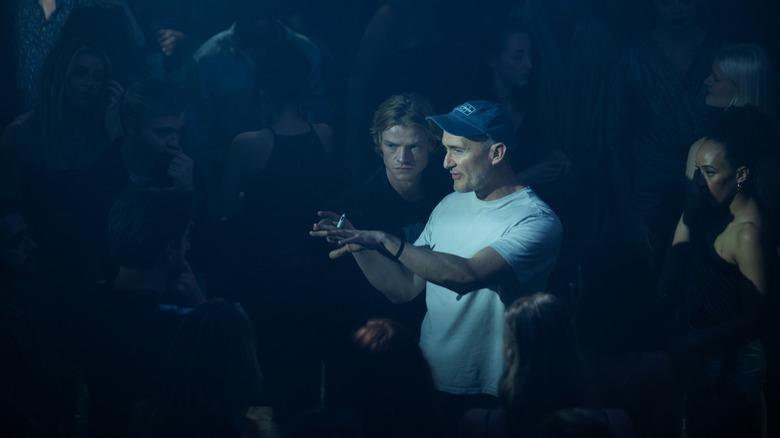 Director James Watkins standing next to Tom Rhys Harries as Matt Hagen on a dance floor surrounded by a crowd of extras in Clayface