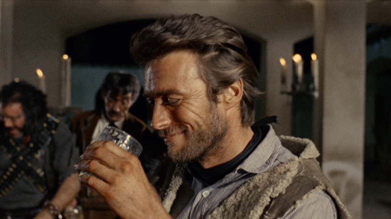Clint Eastwood's Man with No Name smiles as he lifts a glass in A Fistful of Dollars