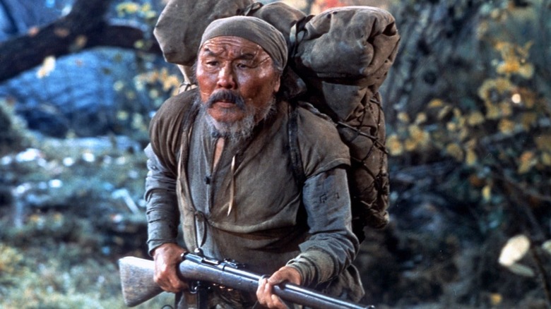 డెర్సు ఉజాలాలోని అడవుల్లో రైఫిల్ మరియు బ్యాక్‌ప్యాక్‌తో డెర్సు