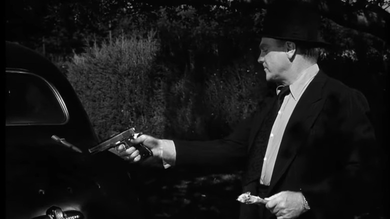 James Cagney's Arthur "Cody" Jarrett holds a pistol as he stands by a car eating chicken in White Heat