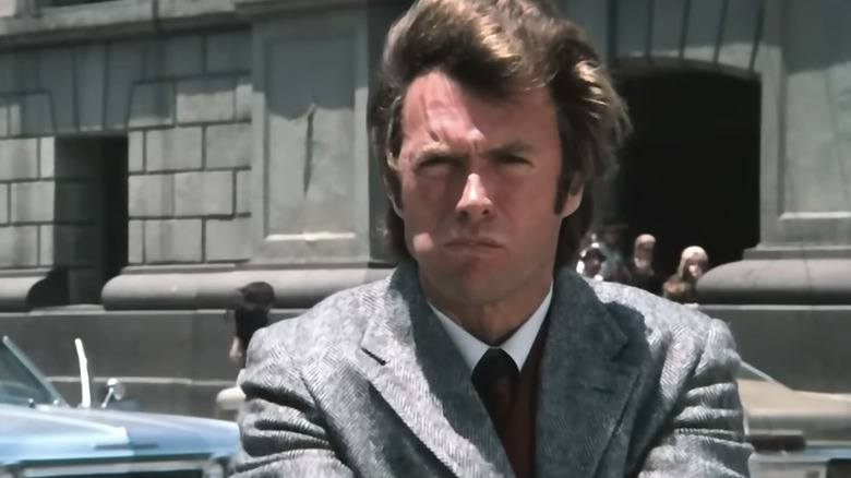 Clint Eastwood's Harry Callahan chews food as he stands in a street in Dirty Harry