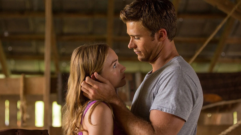 Luke (Scott Eastwood) dengan lembut memeluk wajah Sophia (Britt Robertson) saat mereka saling menatap mata satu sama lain dengan ekspresi yang serius dan penuh kasih di dalam pengaturan pedesaan, seperti gudang dalam perjalanan terpanjang terpanjang