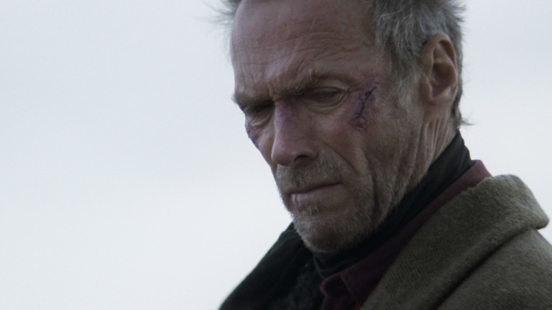 Clint Eastwood's William Munny looks down in closeup against a grey sky in Unforgiven