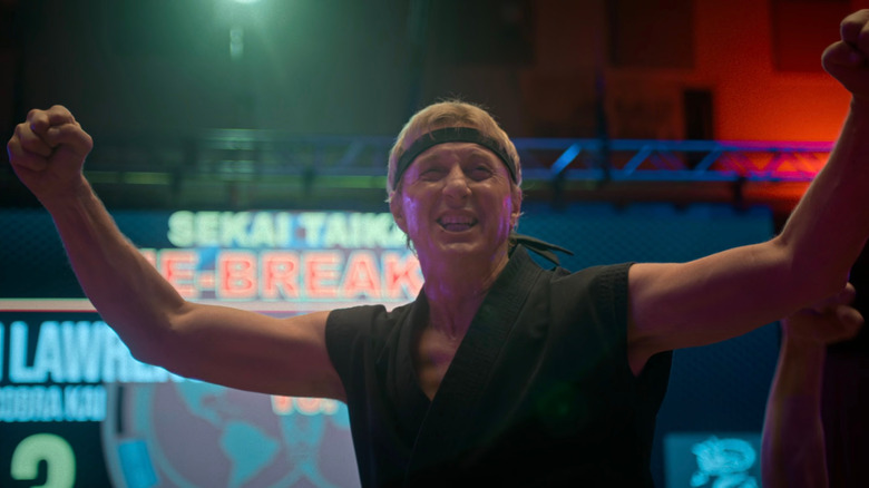 Johnny with his hands up cheering on Cobra Kai