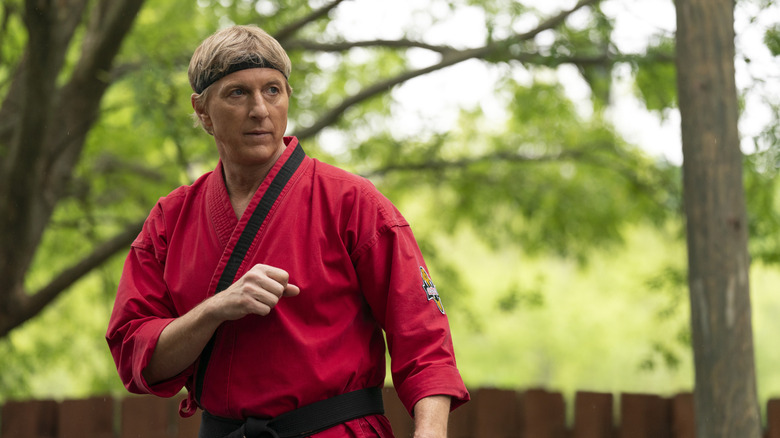 Johnny Lawrence training outside near trees in a red gi in Cobra Kai