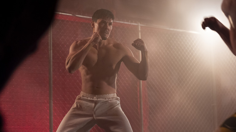 Sensei Wolf in a fighting cage, shirtless, with his fists raised in a fighting position in Cobra Kai