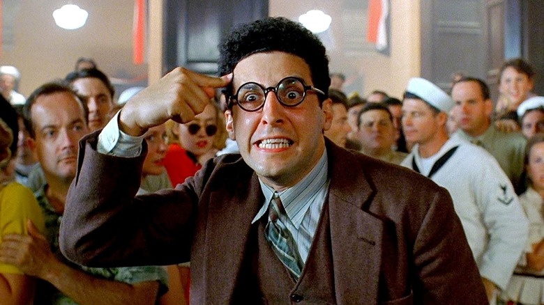 John Turturro as Barton Fink pointing to his temple in a crowd in Barton Fink