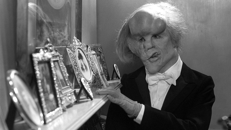 John Merrick looking at a mantlepiece of framed photos in The Elephant Man