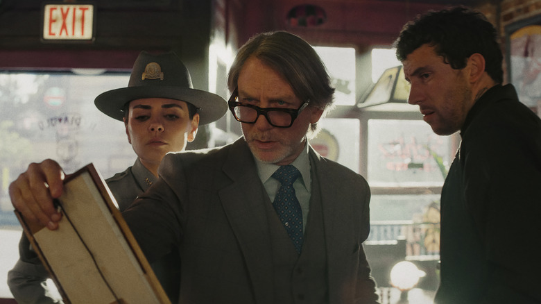 Benoit Blanc, Chief Geraldine Scott, and Father Jud Duplenticy examining a picture in a bar in Wake Up Dead Man: A Knives Out Mystery