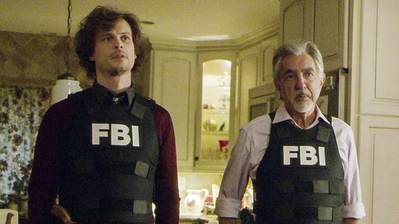 Two of the agents of Criminal Minds stand in a kitchen wearing bullet proof vests
