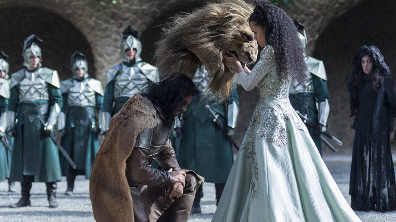 Emerald City's woman holding lion head while soldier kneels