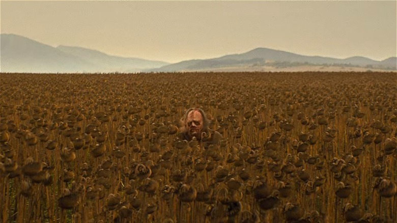 Leatherface sitting in a wilted field of sunflowers
