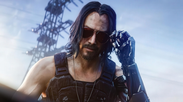 Keanu Reeves as the voice of Johnny Silverhand wearing sunglasses and holding up a prosthetic arm to his face in Cyberpunk 2077