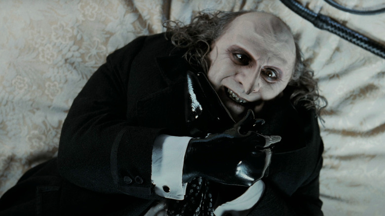 Danny DeVito's Penguin lays on a bed making a bird shape with his hands in Batman Returns