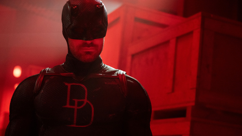 Charlie Cox as Matt Murdock in his Daredevil outfit standing in front of crates bathed in red light in Daredevil: Born Again