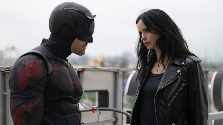 Charlie Cox as Matt Murdock wearing his Daredevil suit and standing on a rooftop next to Krysten Ritter as Jessica Jones in Daredevil: Born Again