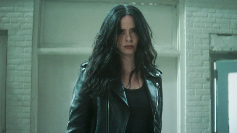 Krysten Ritter as Jessica Jones standing in front of a white wall in Daredevil: Born Again season 2