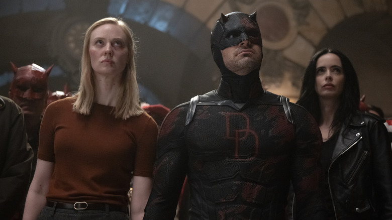 Charlie Cox as Matt Murdock wearing his superhero suit and and standing in front of a mob next to Deborah Ann Woll as Karen Page and Krysten Ritter as Jessica Jones in Daredevil: Born Again