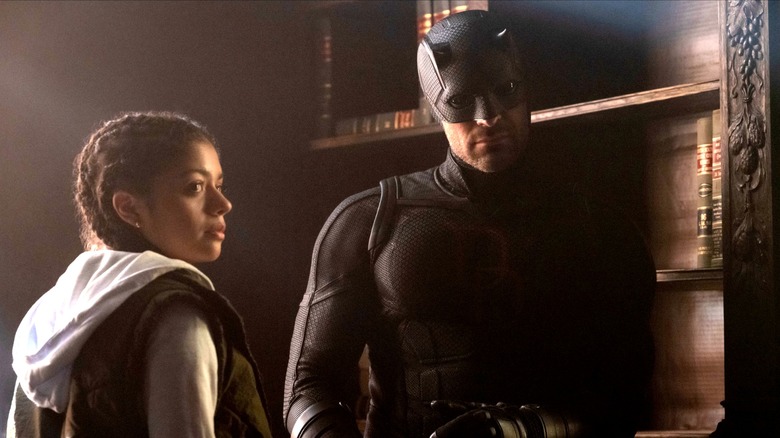 Charlie Cox as Matt Murdock wearing his all-black superhero suit next to Camilia Rodriguez as Angela Del Toro in Daredevil: Born Again