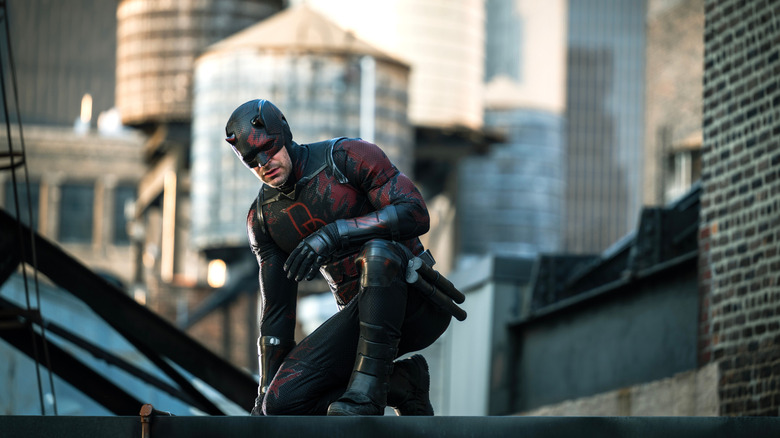 Charlie Cox as Matt Murdock wearing his superhero suit and crouching on a rooftop in New York City in Daredevil: Born Again