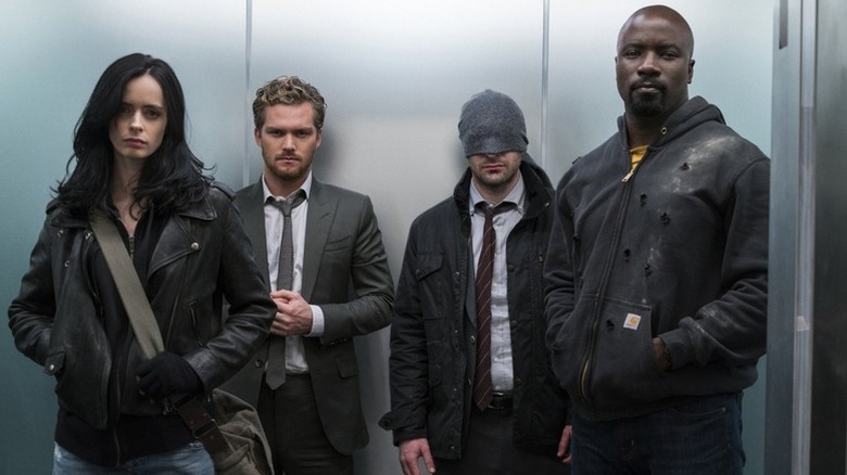 Krysten Ritter as Jessica Jones, Finn Jones as Danny Rand, Charlie Cox as Matt Murdock, and Mike Colter as Luke Cage standing together in an elevator in "The Defenders" miniseries