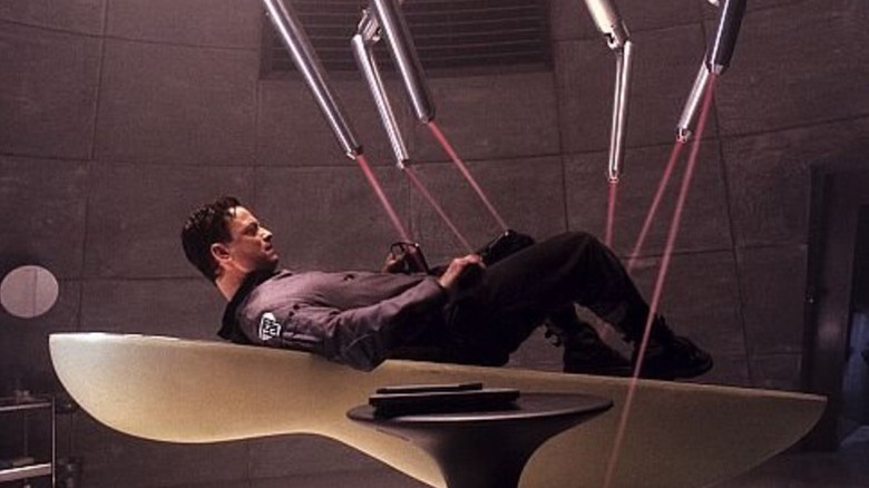Spencer Olham laying on a futuristic medical table with lasers all around him in Impostor