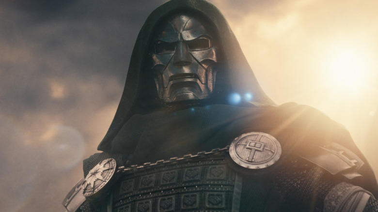 Robert Downey Jr. as Victor von Doom wearing a mask and hood and spreading his arms in a threatening pose in Avengers: Doomsday