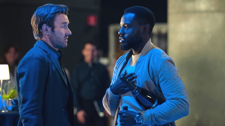 Joel Edgerton as Jason2 standing next to Dayo Okeniyi as Leighton Vance as he holds two bottles of champagne in Dark Matter