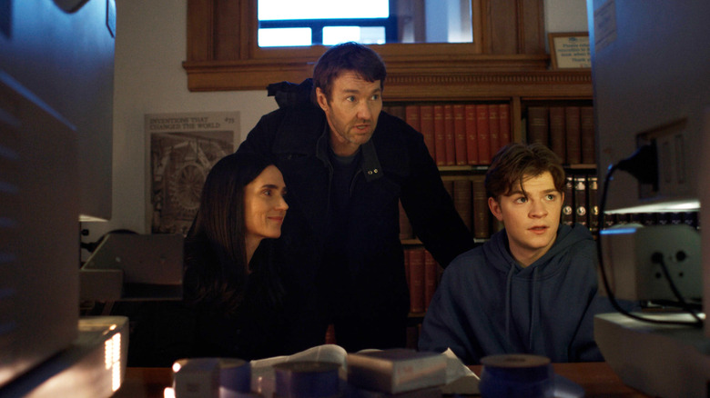 Joel Edgerton as Jason Dessen standing behind Jennifer Connelly as Daniela Dessen and Oakes Fegley as Charlie Dessen in a library in Dark Matter