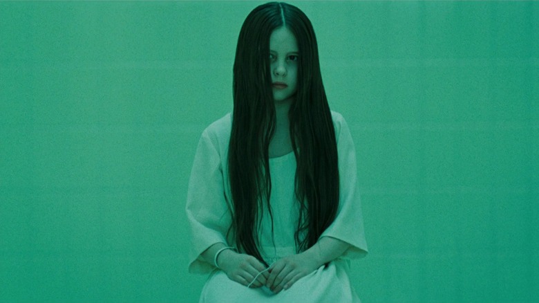 Daveigh Chase as Samara Morgan wearing white and sitting in a chair in a famous scene from The Ring