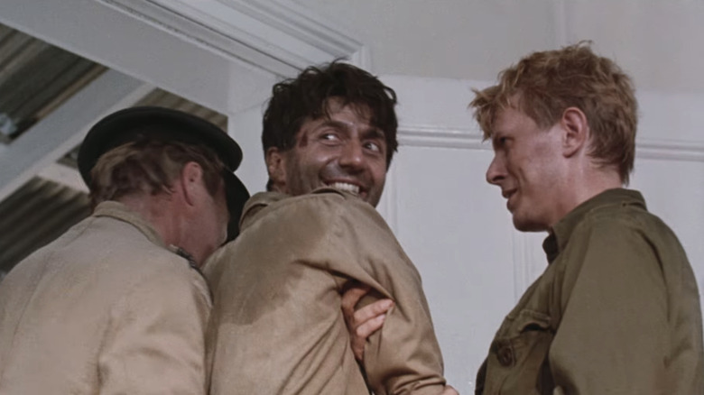 Tom Conti's Lieutenant-Colonel John Lawrence smiles as David Bowie's Maj. Jack "Strafer" Celliers escorts him out of a room