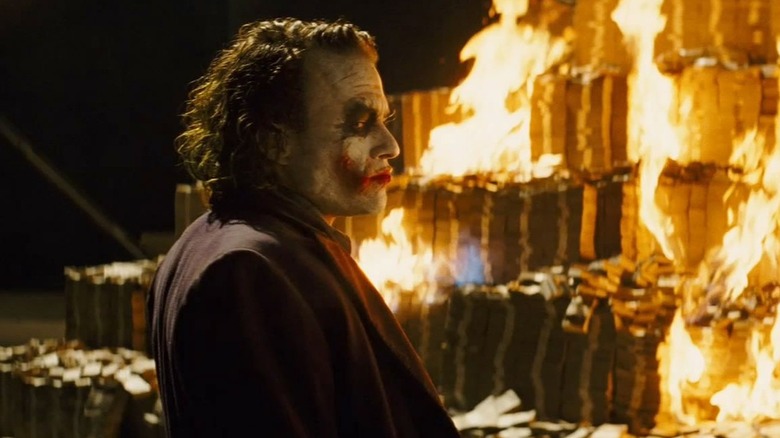 Heath Ledger as the Joker watching a pile of money burn in The Dark Knight