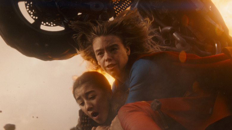 Milly Alcock as Supergirl protecting Eve Ridley as Ruthye as a motorcycle flies over them in Supergirl (2026)