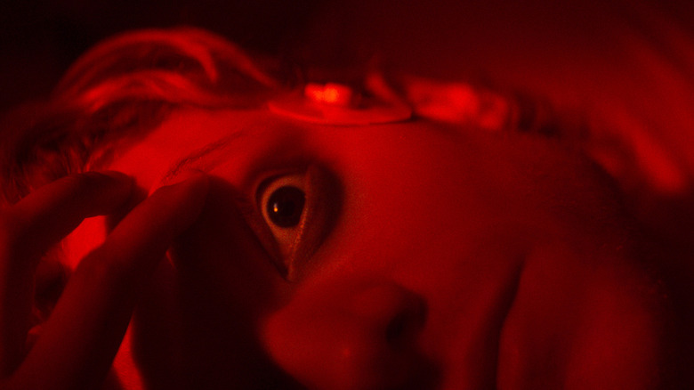 Matt Hagen is bathed in red light with an electrode attached to his temple and his eye wide open in a shot from Clayface