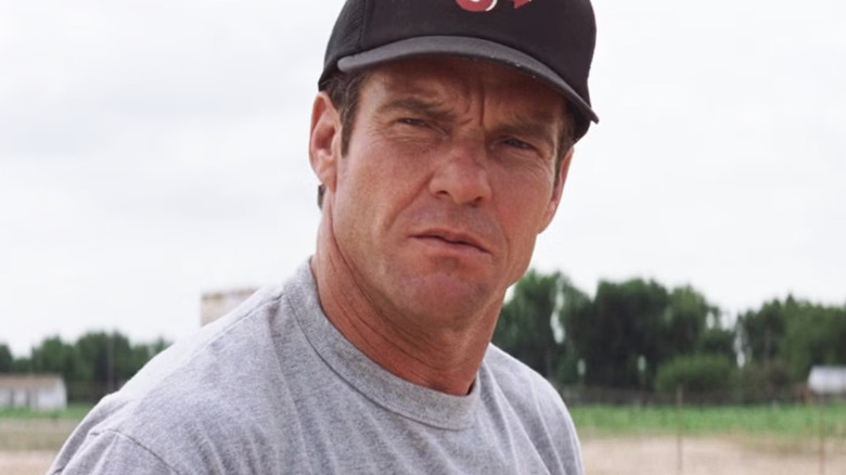 A close-up of Dennis Quaid as Jimmy Morris standing on a baseball field, squinting intensely while wearing a baseball cap in a scene from The Rookie
