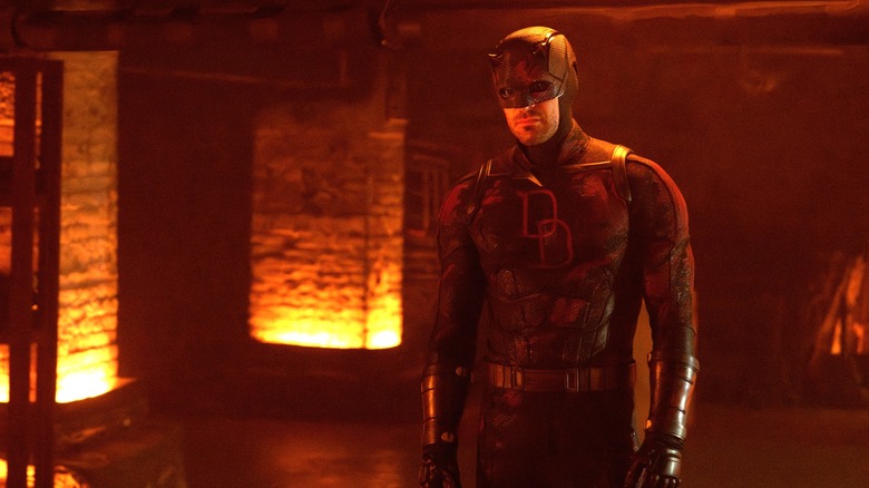 Charlie Cox as Matt Murdock wearing his Daredevil suit in a room bathed in orange light in Daredevil: Born Again