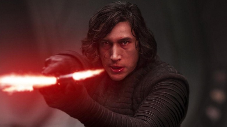 Adam Driver as Kylo Ren holding his lightsaber out in front of him in Star Wars: The Force Awakens