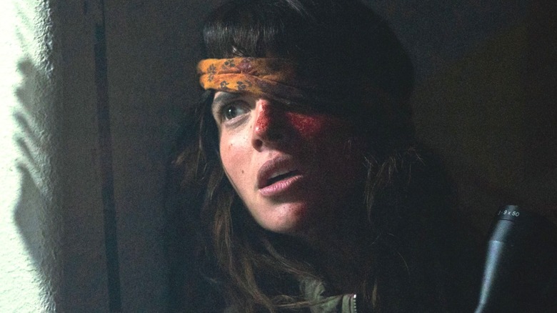 Celeste looks out a window with one eye under a bandana while wielding a weapon in Onslaught