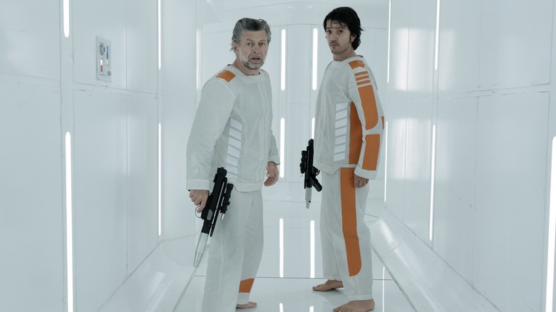 Andor and Kino Loy stand with blasters in the prison hallway