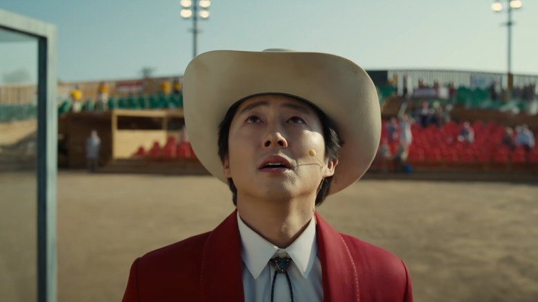 steven yeun looking up at the sky in a beige cowboy hat and red suit in the movie nope