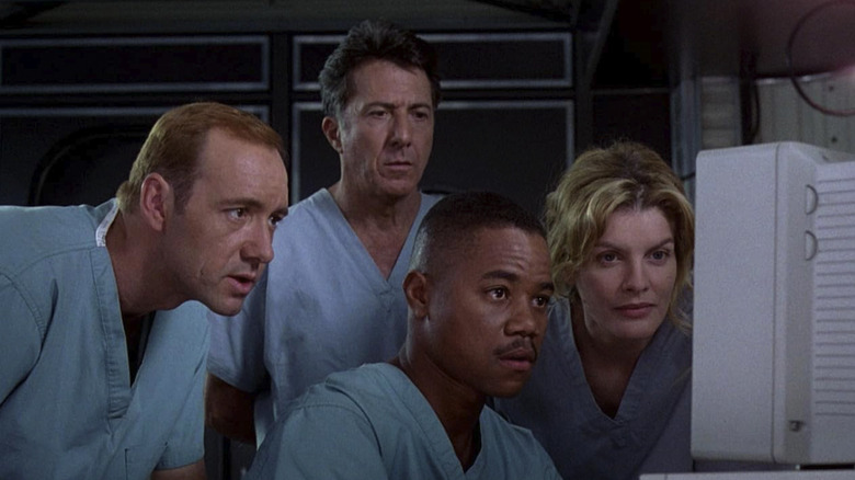 Sam Daniels looking concerned in Outbreak as he looks at a computer screen with his colleagues