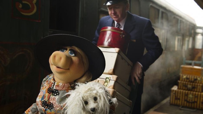 Miss Piggy carrying her dog while her butler carries her bags through a train station in Muppets Most Wanted